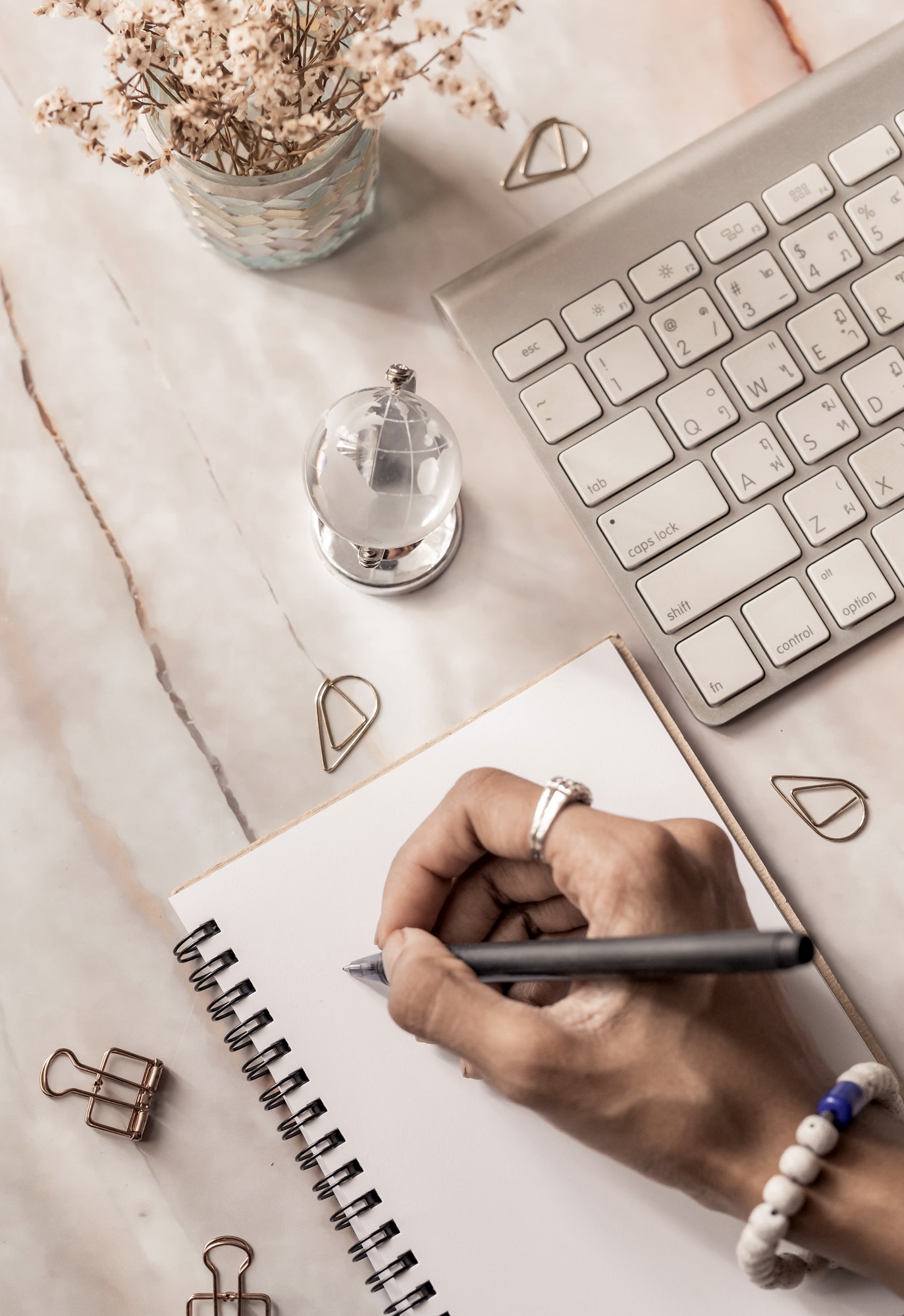A woman’s hand about to write in a notebook, top view of desk